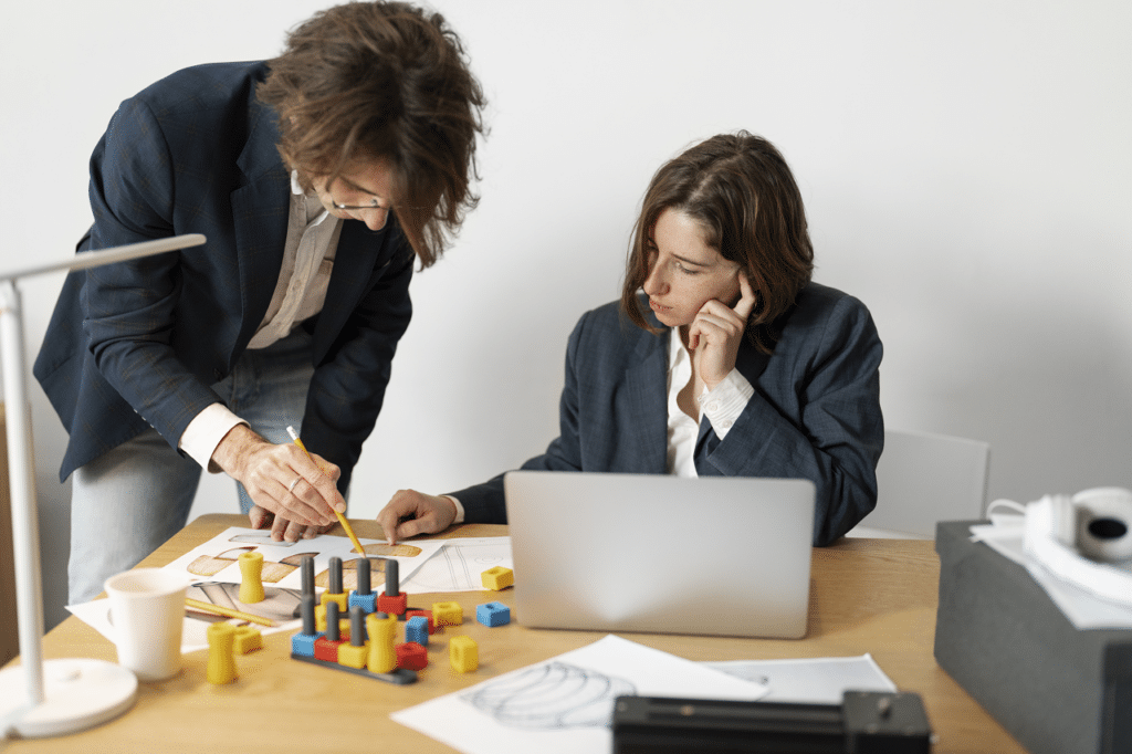 Two engineers working together at a desk, reviewing documents and using models, illustrating the Engineering Method of Problem Solving.