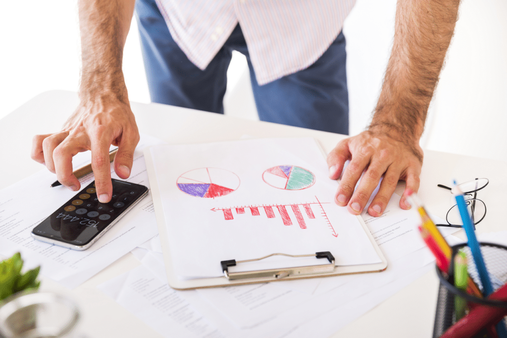 A person using a calculator while examining charts and graphs on a clipboard, illustrating Effective Cost Reduction Strategies in Production.